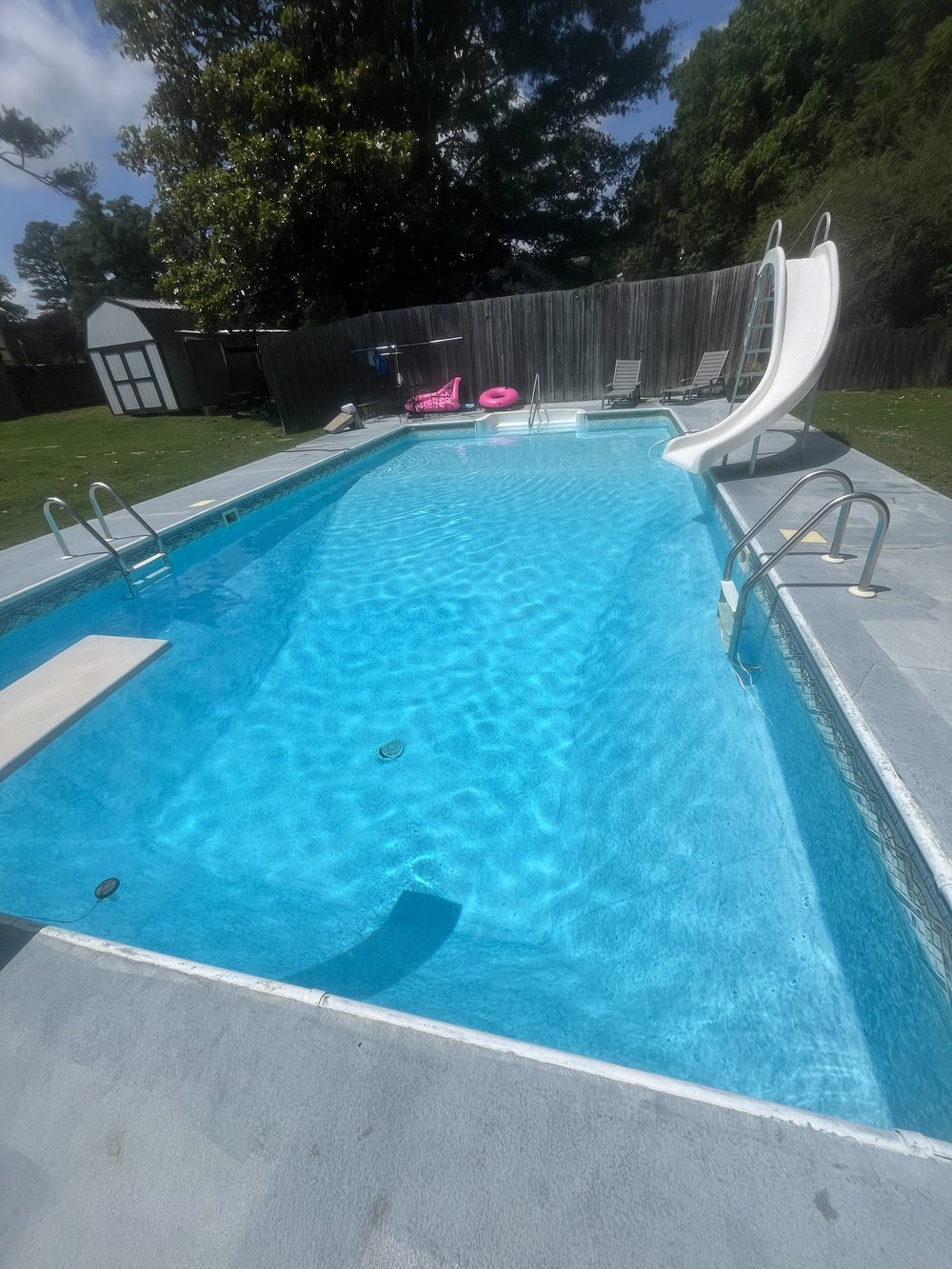 Clear backyard pool with a diving board and slide